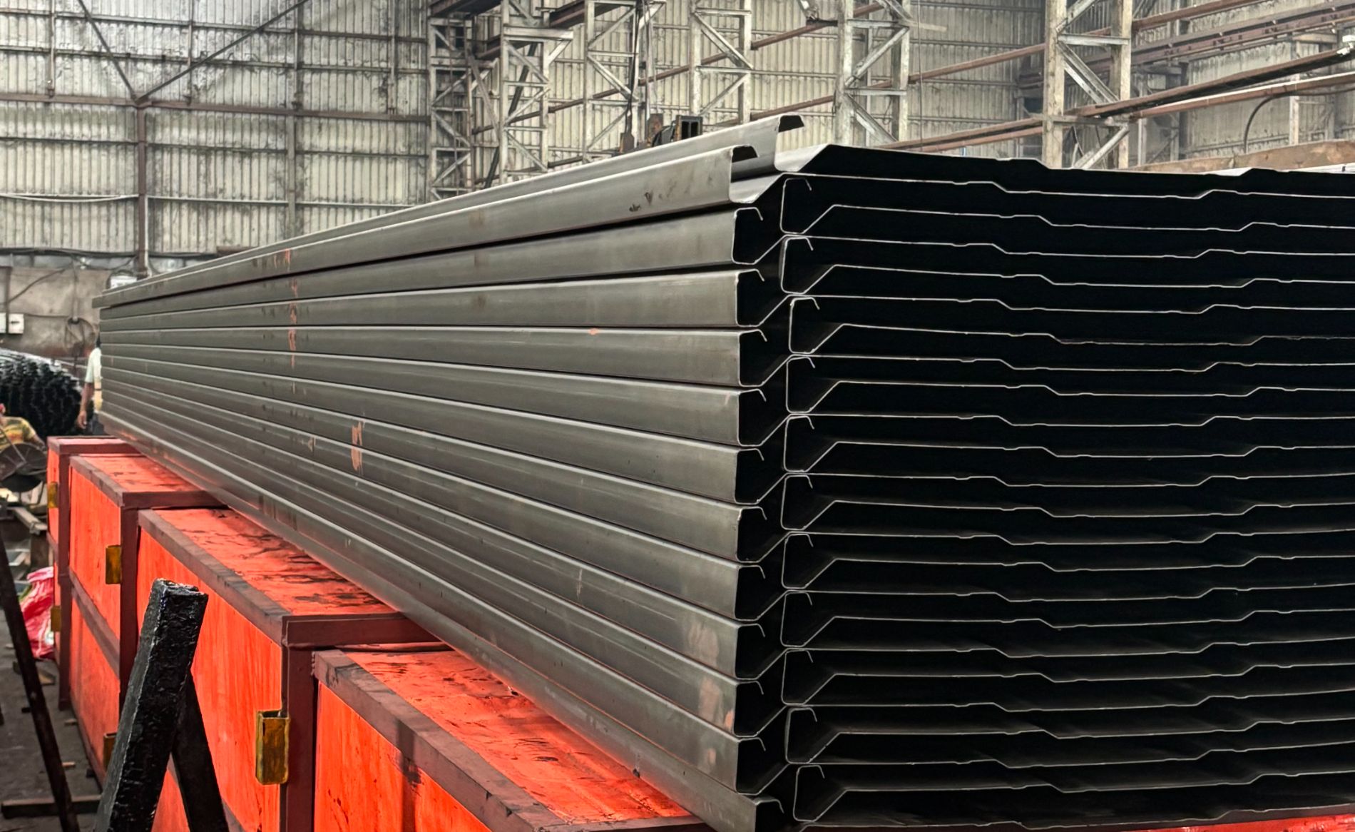 Roll formed ESP collecting electrodes stacked in the fabrication shop, profile geometry visible along the full plate length