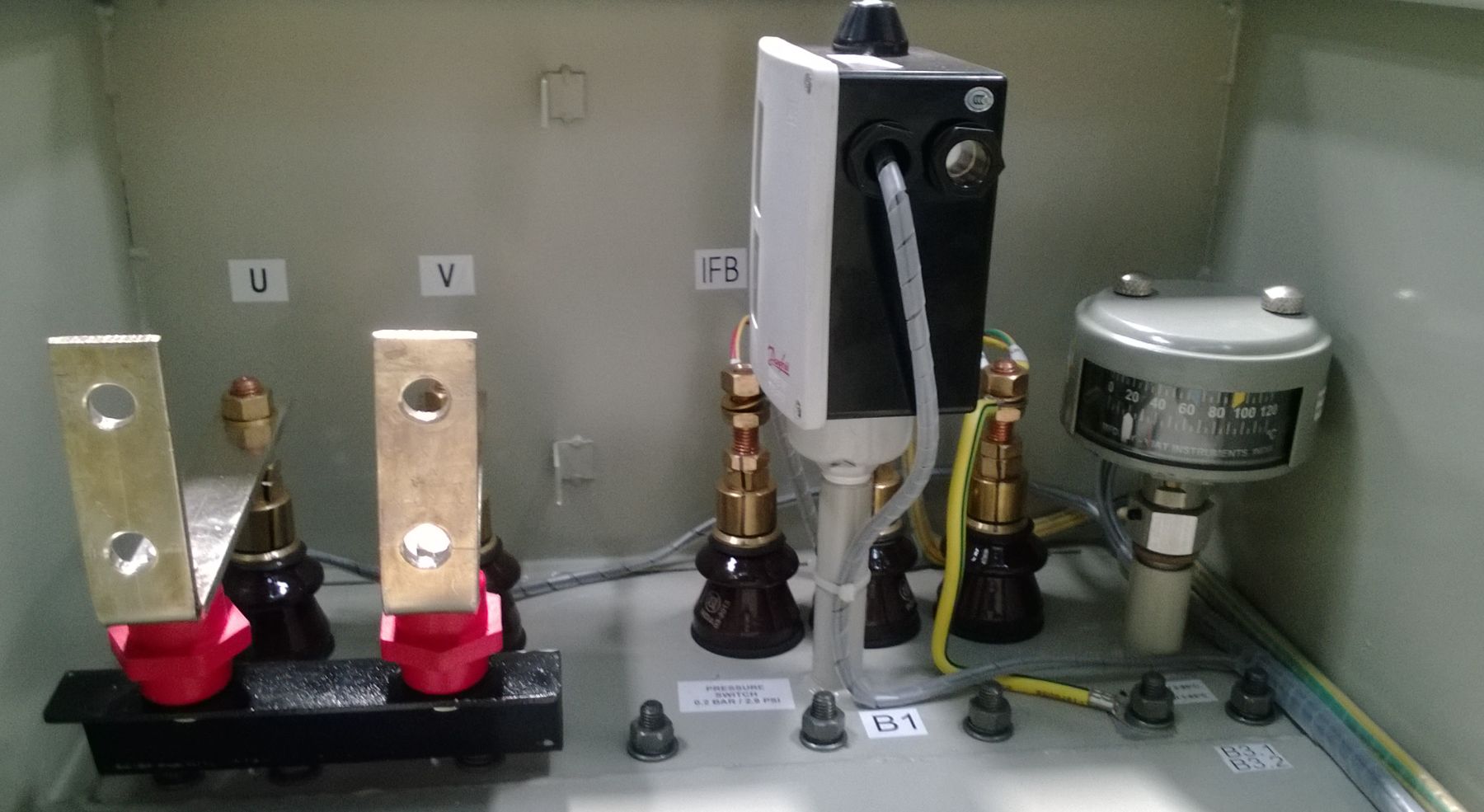 Transformer rectifier terminal box interior showing the LT bushings and busbar links, the pressure switch and the oil temperature indicator