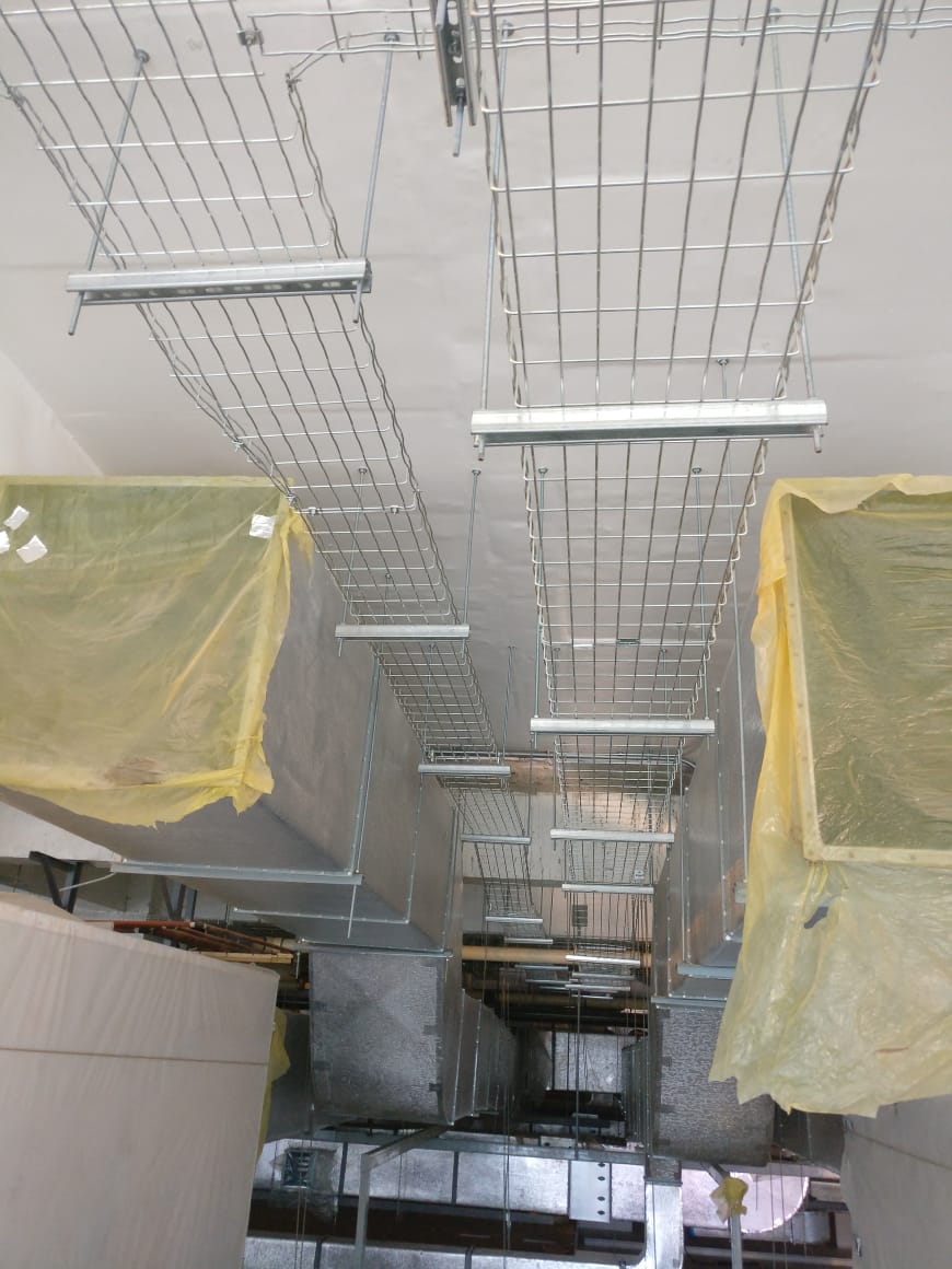 Multiple levels of wire mesh tray suspended below a ceiling alongside lighting and services