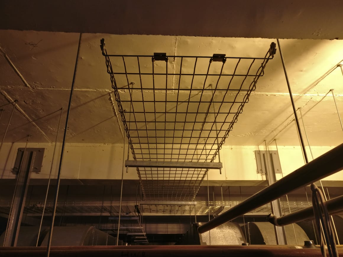 Wire mesh tray suspended from a ceiling on twin hangers with connecting clamps